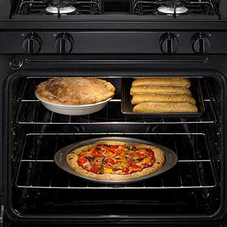A pizza bakes on the bottom rack in the oven with a pie and breadsticks above it on the upper rack.