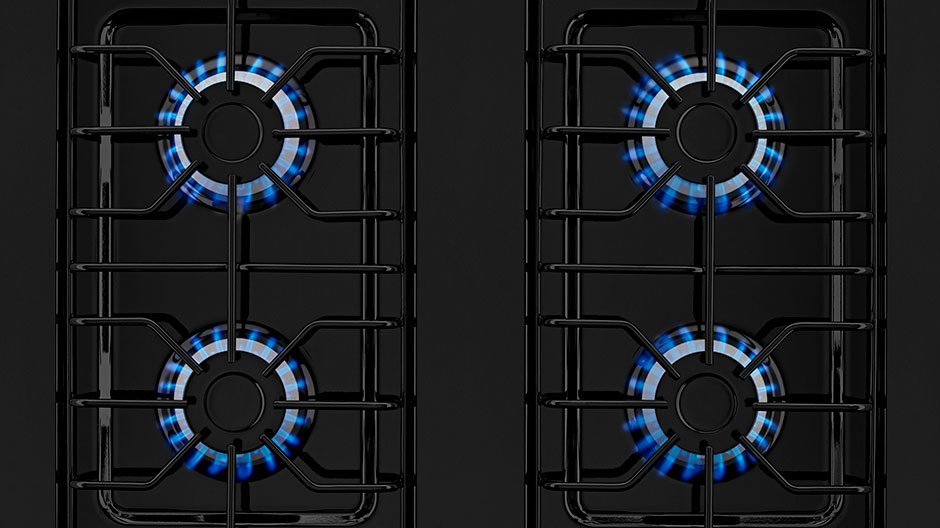 All four gas burners are lit to show their blue flames against the black cooktop and grates.