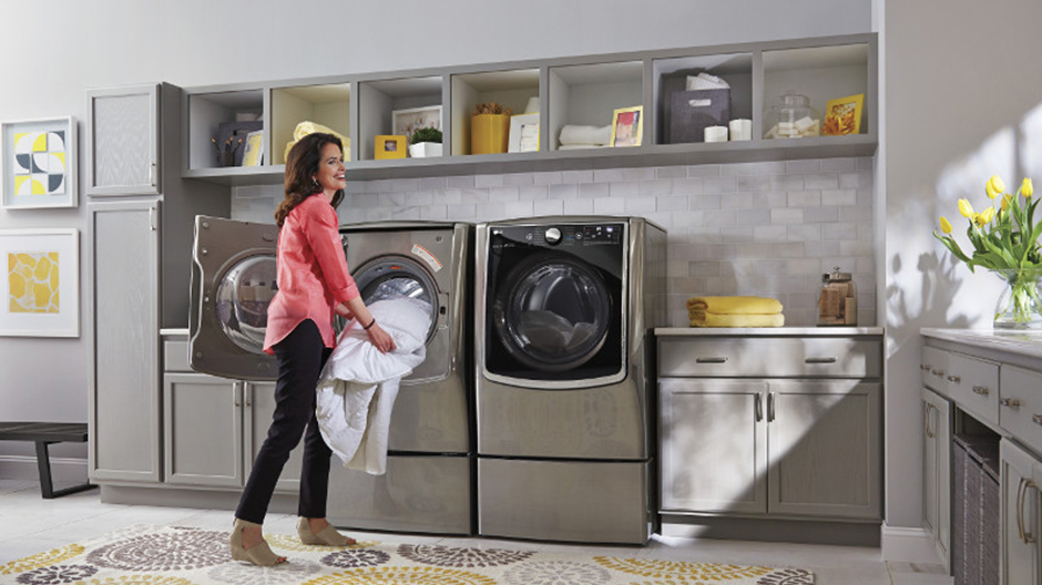 Woman in bright, modern laundry room loads a white comforter into an LG front load washer thatÕs part of a washer and dryer set