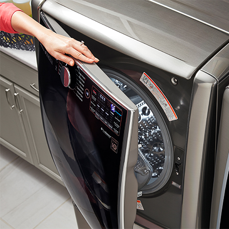 Top down view of a woman's arm opening up an LG washing machine with 10 Year Warranty sticker visible