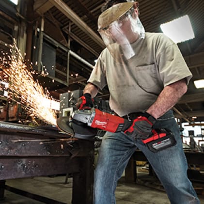 Man wearing gloves and face shield uses the M18 FUEL Braking Grinder on metal as sparks fly.