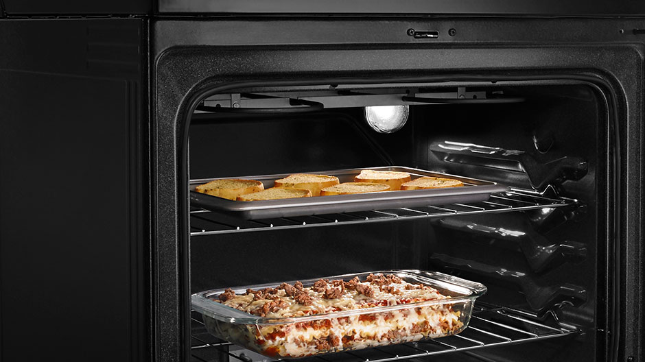 The oven door is open, revealing garlic bread baking on the upper rack and lasagna baking on the lower rack.