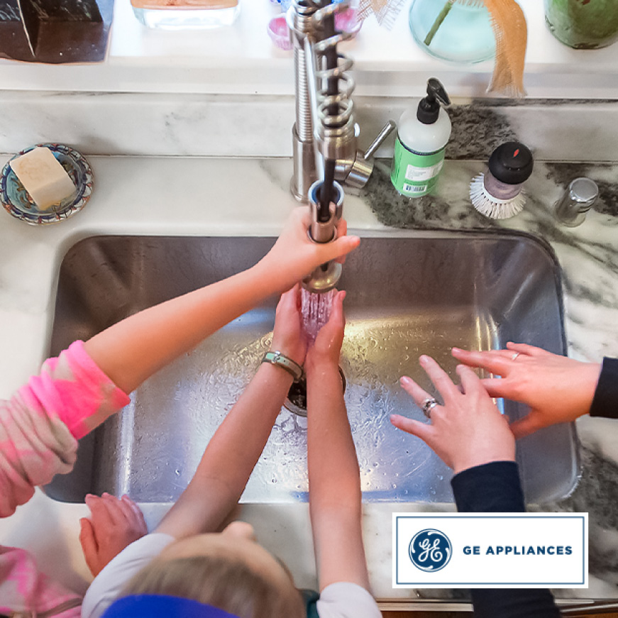 A family washes their hands together in the kitchen sink. A family washes their hands together in the kitchen sink.