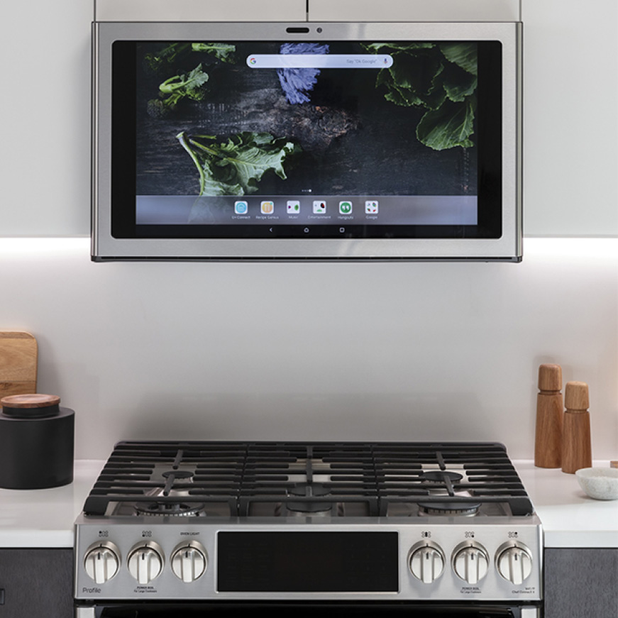 A front view of the kitchen hub over a range. The home screen is displayed on the kitchen hub. A front view of the kitchen hub over a range. The home screen is displayed on the kitchen hub.