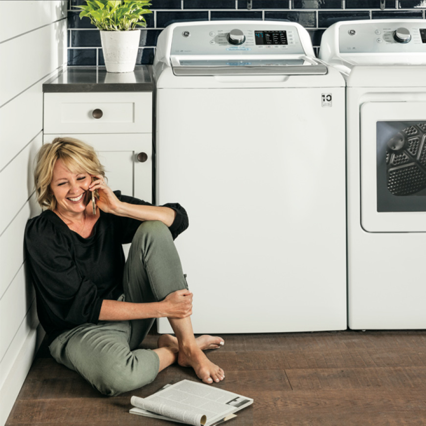 Woman sitting next to quiet washer reading a magazine while on the phone