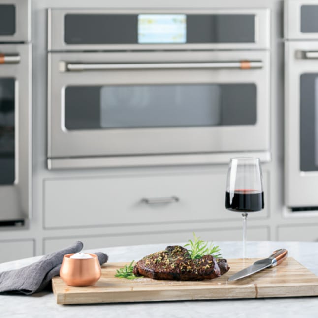 An adaptable advantium oven is installed between two larger wall ovens. A meal on a wooden tray is arranged on a counter in front of the oven.