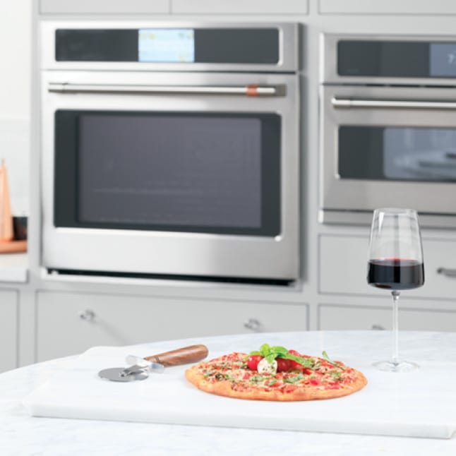 A gourmet pizza and a glass of wine rest on a marble slab in front of the wall oven.