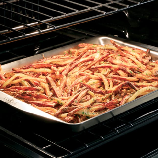 Seasoned fries in a metal tray are cooked to a crispy golden brown in a Cafe stove.