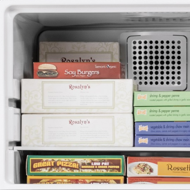 A variety of frozen foods are stacked neatly in the freezer compartment on glass shelves.