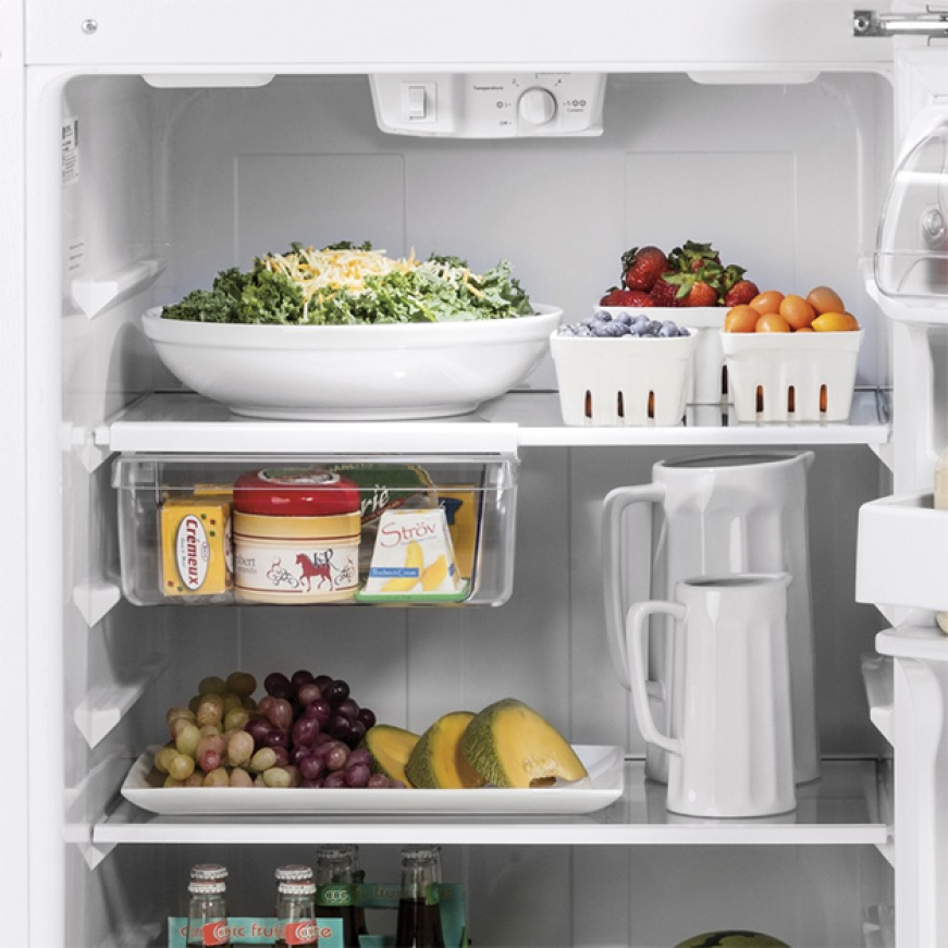 The open fridge is filled with a variety of foods on the glass shelving.